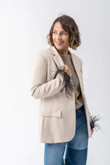 Blazer color beige con solapas de muesca, cierre frontal con un botón y bolsillos de parche. Las mangas largas están adornadas con plumas negras.