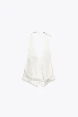 Top chaleco blanco de tejido satinado con cuello halter ajustable con hebilla metálica, falsos bolsillos de doble vivo en delantero, espalda descubierta con tira ajustable y cierre frontal con botones.