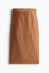Pollera midi color marrón, de tejido transparente en mezcla de lyocell, tiro alto, bajo recto, tajo trasero y viso corto.