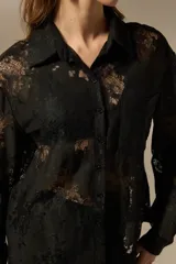Camisa negra de poliamida con diseño calado de encaje floral, corte holgado, cuello camisero, botones frontales y mangas largas.