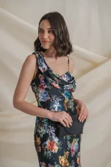 Vestido largo de satén de seda negro con estampado de flores de colores. Tiene escote irregular drapeado, un bretel ancho y otro fino con manga caída.