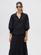 Camisa de broderie de algodón color negro, con cuello mao y cierre de cuatro botones. Presenta mangas abullonadas y galones con transparencias en la parte delantera y mangas.