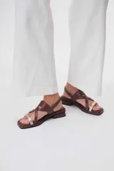 Sandalias bajas de cuero color marrón con tiras cruzadas y detalle de tira delgada color rosa.