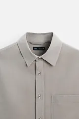 Camisa color crema de corte relaxed fit, confeccionada en tejido de mezcla de algodón suave al tacto. Tiene cuello solapa, manga larga con puños abotonados, un bolsillo de parche en el pecho y cierre frontal con botones.