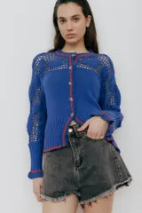 Cárdigan azul de algodón con calce entallado, tejido acanalado y detalles de crochet. Tiene mangas con volados y vivos rojos en cuello, puños y frente.