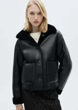 Chaqueta corta negra de cuero sintético con cuello y puños de piel sintética. Cierre frontal con botones y bolsillos de parche.