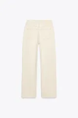 Pantalón de jean color crudo, de tiro alto, corte recto y largo tobillero. Tiene cinco bolsillos, cierre frontal con cremallera y botón metálico.