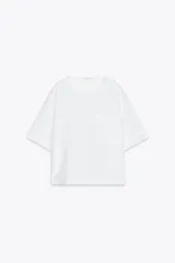 Blusa blanca de lino 100% con cuello redondo, manga corta, bolsillo de parche en el pecho y bajo asimétrico con aberturas laterales.