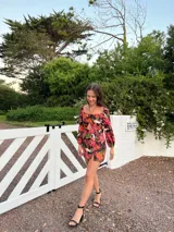 Vestido corto con estampado floral en tonos rosa y lila, escote cuadrado con detalle fruncido y abertura en el centro, mangas largas abullonadas y falda con tajo lateral.