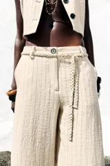 Pantalón de tiro alto color beige con finas rayas verticales negras, pernera ancha y cinturón trenzado a tono.