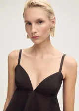 Top negro con tirantes finos, escote en pico y bajo con volantes. Cierre de gancho en la parte posterior y abertura en la espalda.