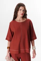 Blusa de lino color beige claro, con mangas 3/4 y cuello redondo. Presenta pespuntes a contratono en el centro, puños y ruedo.