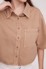 Camisa color verde oliva oscuro, de corte cropped y holgado, con cuello clásico, manga corta y bolsillo en el pecho.