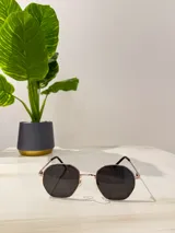 Lentes de sol con marco octogonal dorado y lentes oscuros.