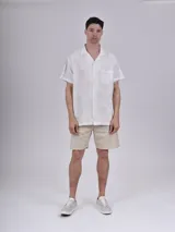 Camisa de manga corta con estampado de hojas color verde sobre fondo beige, cuello solapa y bolsillo en el pecho.