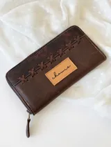 Billetera de cuero marrón con cierre metálico y diseño de cruces cosidas en el frente. Incluye monedero interno y espacio para billetes extendidos.