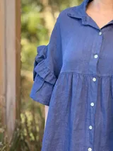 Vestido camisero azul de lino italiano, con cuello camisero, botones frontales, mangas 3/4 con doble volado y bolsillos laterales.