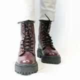 Bota de cuero negra con caña media, cordones y plataforma track. Presenta apliques de tachas plateadas en el lateral exterior.