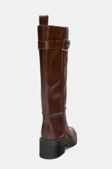 Bota alta de cuero sintético color marrón oscuro, con caña recta y punta cuadrada. Presenta pespuntes a contraste en las uniones y un detalle de correa con hebilla metálica en la parte superior. Posee un tacón de bloque de altura media.