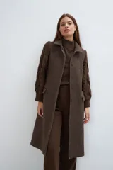 Tapado largo y recto color marrón con mangas tejidas con diseño de trenzas. Tiene cuello solapa, cierre frontal con botones ocultos y bolsillos con solapa. Con forro.