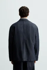 Blazer azul oscuro de denim, corte relaxed fit, con cuello de solapas de muesca, manga larga con puños abotonados, bolsillos de solapa en la cadera, abertura en el centro de la espalda y cierre frontal con botones.