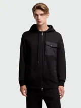 Buzo negro con capucha y cierre frontal completo. Presenta un bolsillo tipo parche en el pecho confeccionado en tejido técnico.