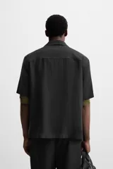 Camisa negra de corte relaxed fit, confeccionada en tejido con mezcla de modal. Tiene cuello bowling, manga corta, bolsillo de parche en el pecho y cierre frontal con botones.