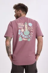 Remera de algodón color verde salvia, con cuello redondo y manga corta. Presenta un pequeño parche estampado en el pecho con un diseño gráfico.