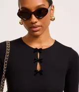 Blusa blanca de mangas cortas, confeccionada en Rib, con cuello redondo y lazos de terciopelo negros uniendo la abertura en la parte de abajo.