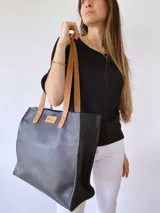 Bolso tipo tote bag de cuero negro con forro de tela, doble asa de cuero color suela, bolsillo frontal y bolsillo interno.