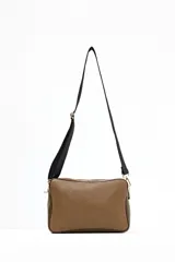 Bandolera rectangular con cuerpo principal de eco-piel texturizada color marrón topo y bolsillo frontal con estampado de vaca (marrón y blanco). Posee correa ajustable ancha de tela negra y herrajes dorados.