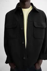 Sobrecamisa color beige de corte relaxed fit, con cuello solapa, manga larga con puños abotonados, bolsillos de plastrón con solapa en el pecho y bolsillos de vivo en la cadera. Cierre frontal con botones.
