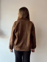 Campera marrón de gamuza con cuello clásico, cierre frontal con cremallera y bolsillos con solapa y botón.