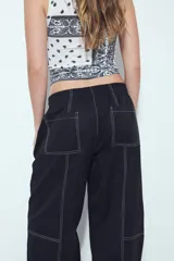 Pantalón tipo babucha negro de tiro bajo con costuras visibles en contraste blanco. Presenta cintura elástica con lazo ajustable blanco y silueta amplia con caída relajada.
