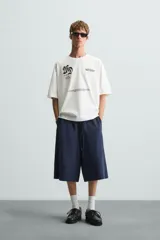 Camiseta blanca de corte holgado, cuello redondo y manga corta. Presenta estampados combinados en negro en la parte delantera y trasera.