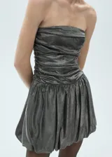 Vestido corto plateado con brillos, sin mangas, con escote palabra de honor, diseño drapeado y falda globo.