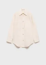 Camisa color crema de corte oversize, con cuello camisero, mangas largas con puños abotonados, cierre frontal con botones, costuras decorativas y bordados florales en los hombros.