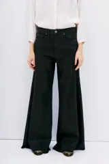 Pantalón de jean negro de corte oxford, tiro medio, con cintura y cadera ajustadas, y piernas anchas con recortes laterales.