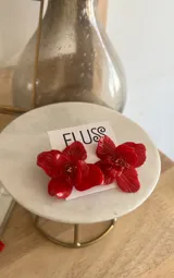 Par de aros artesanales con forma de flor roja, hechos en porcelana con centro dorado y perno de acero.