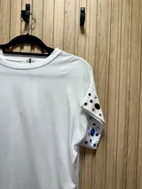 Remera blanca de algodón de manga corta con cuello redondo y apliques de pedrería de colores en las mangas.