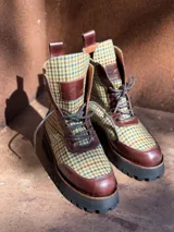 Botas de caña media con plataforma, confeccionadas en tweed a cuadros rojos y negros, con detalles en cuero marrón y cordones marrones.
