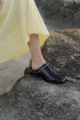 Mules de cuero negro con punta cuadrada y detalle de tachas plateadas en el borde superior.