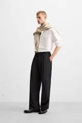 Pantalón negro de corte ancho con cinturón de tela con hebilla metálica y pliegues frontales.
