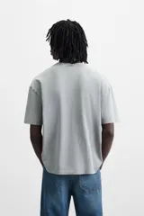 Camiseta gris con cuello redondo y manga corta. Presenta estampados, bordados y parches frontales combinados a contraste. Tiene un efecto lavado.