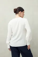 Camisa celeste de manga larga con cuello redondo y escote en V. Presenta detalles de pasamanería en el frente y las mangas, y botones forrados al tono. De corte fluido.