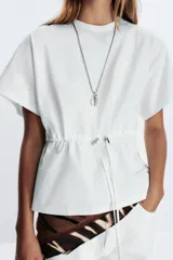 Camiseta color crudo de algodón con cuello redondo, manga corta caída y cintura ajustable con cordón.