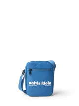 Cartera tipo reporter de Calvin Klein, color azul vibrante, con correa ajustable para llevar cruzada. Presenta un bolsillo exterior con cierre en la parte frontal y un bolsillo interior con ranura. El diseño destaca por el logo gráfico de Calvin Klein en blanco con texto adicional que indica "West 39th Street" y "New York City".