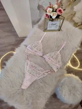Conjunto de lencería de encaje floral en tonos rosa y crema, compuesto por un corpiño triangular sin aro con breteles finos regulables y una tanga regulable.