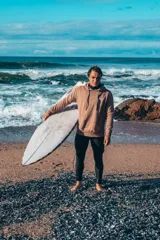 Buzo hoodie marrón con capucha y cordones ajustables. Estampado en la espalda con la frase "Glassy Waves", "Good Vibes", una flor y las fechas "1971, 1982, 1993".