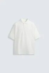 Polo blanco de piqué con corte relaxed fit, cuello con solapa y cierre frontal con botones, y mangas cortas.